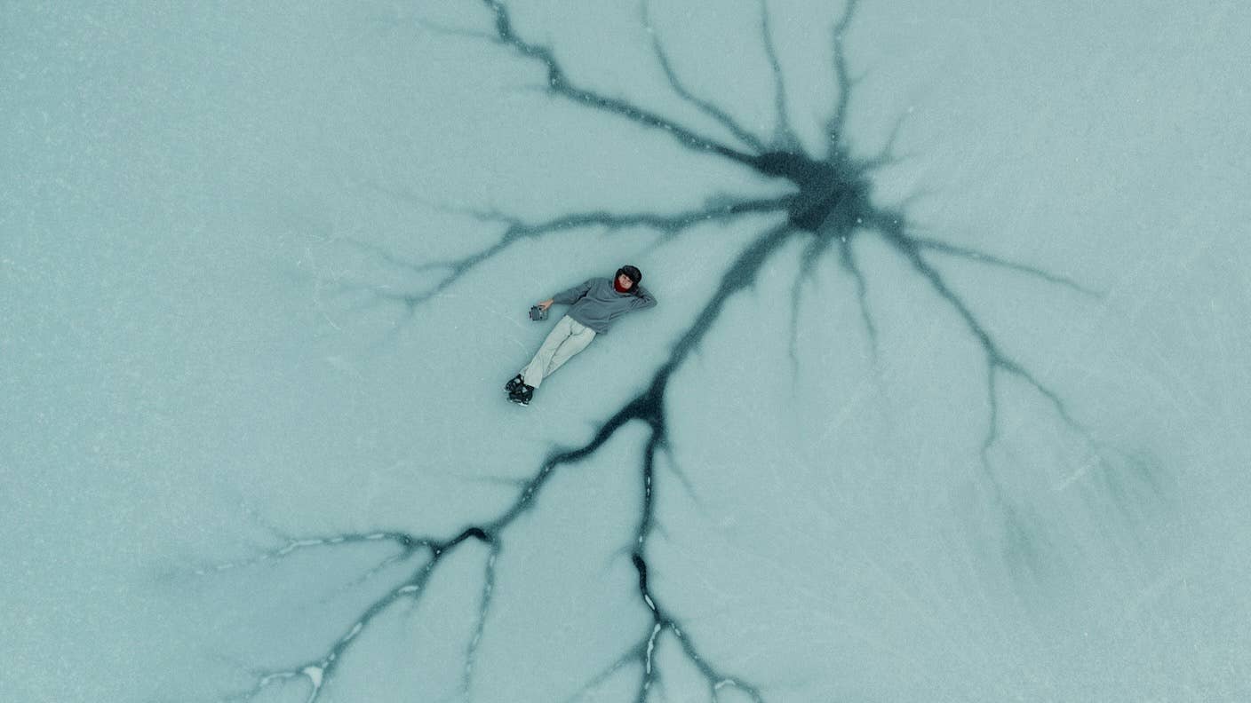 Parkinson’s Patients Say Their Symptoms Eased After Receiving Millions of New Brain Cells A person is lying down on ice, surround by cracks that resemble a neuron
