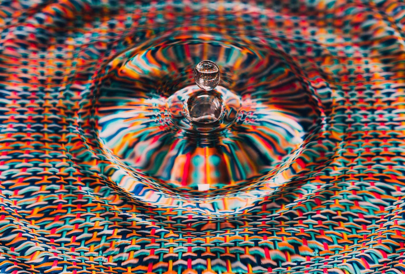 A drop of water over rippling surface and a woven textile beneath.