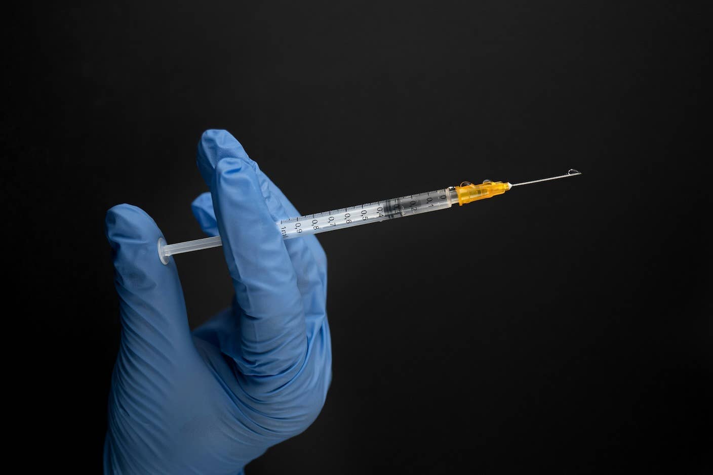 A blue-gloved hand holds a needle