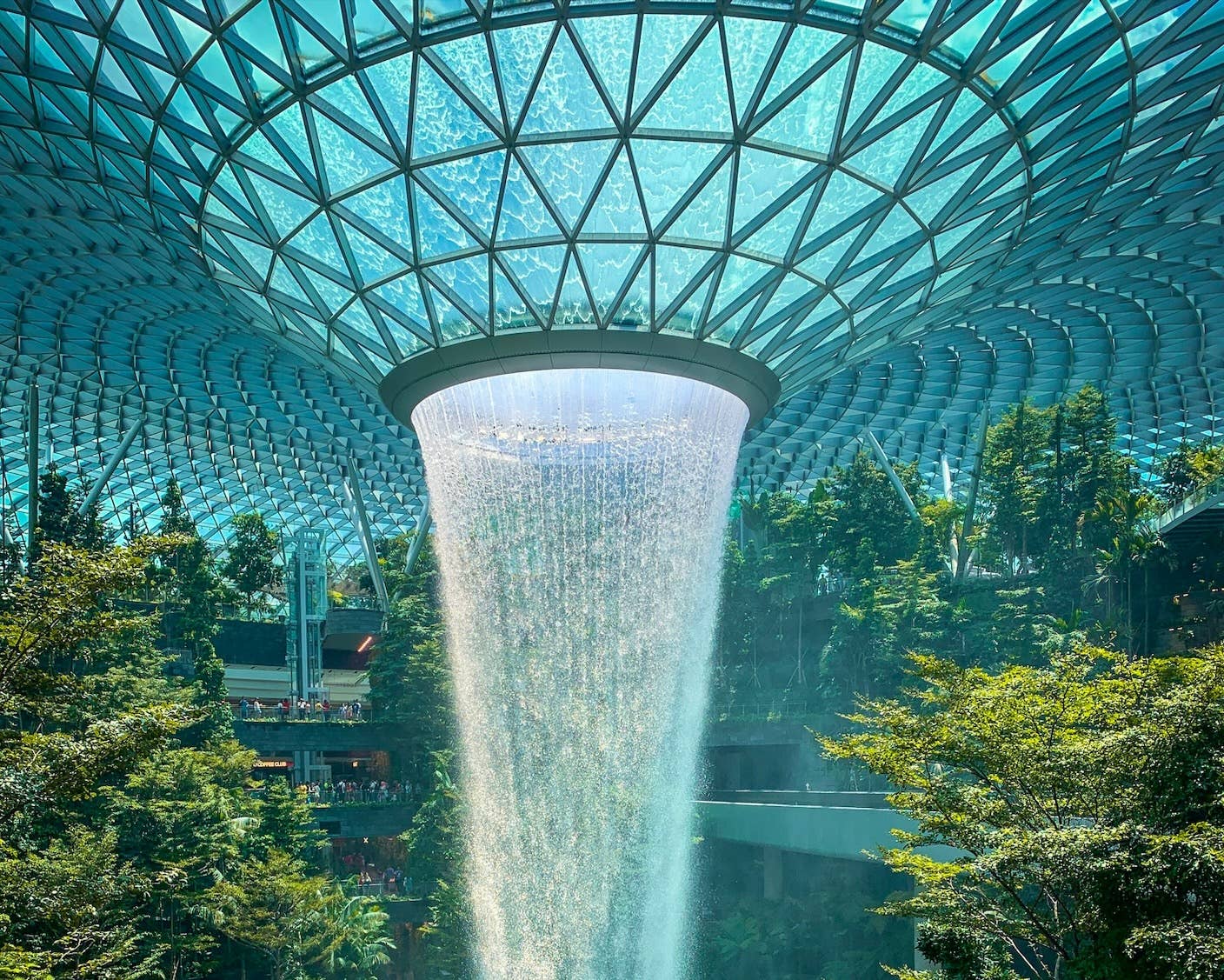 A futuristic waterfall falls from an architectural roof into a verdant green space