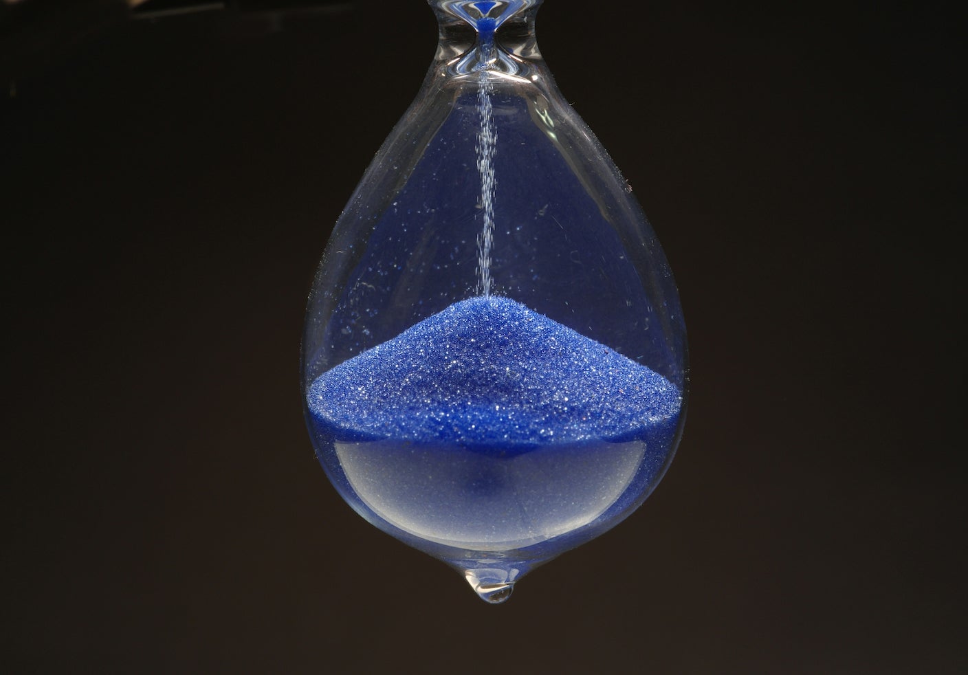 Grains of blue sand falls through an hour glass
