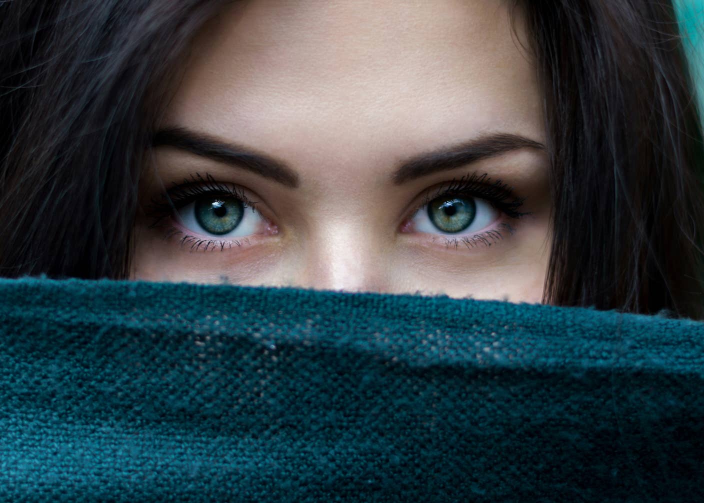 What We Actually See—and Don’t See—Shows Consciousness Is Only the Tip of the Iceberg A woman with green eyes and dark hair peeks above a blue-green scarf
