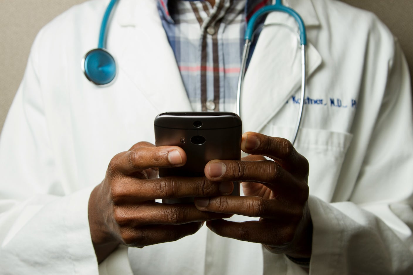 A doctor with a stethoscope and white coat consults a phone