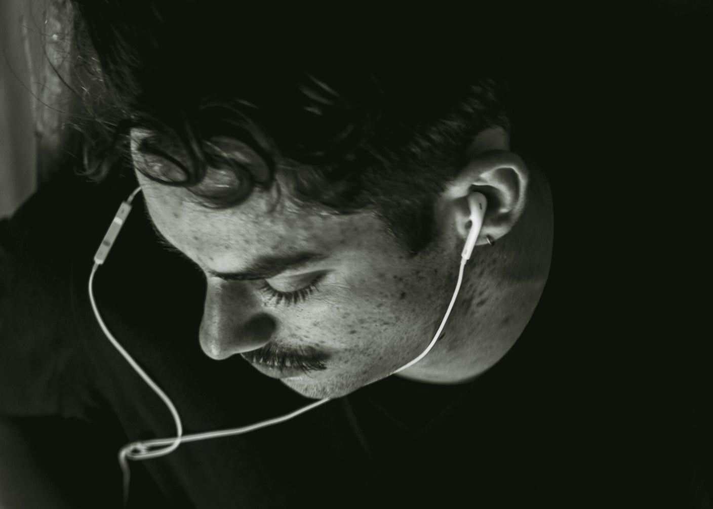 A man wearing wired earbuds with eyes closed