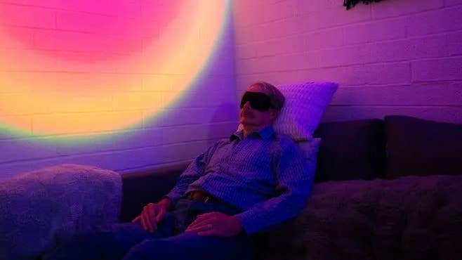 Can Psychedelics Reboot Aging Brains? We’re About to Find Out A man on a couch with eyes covered. Colorful lights on the wall.