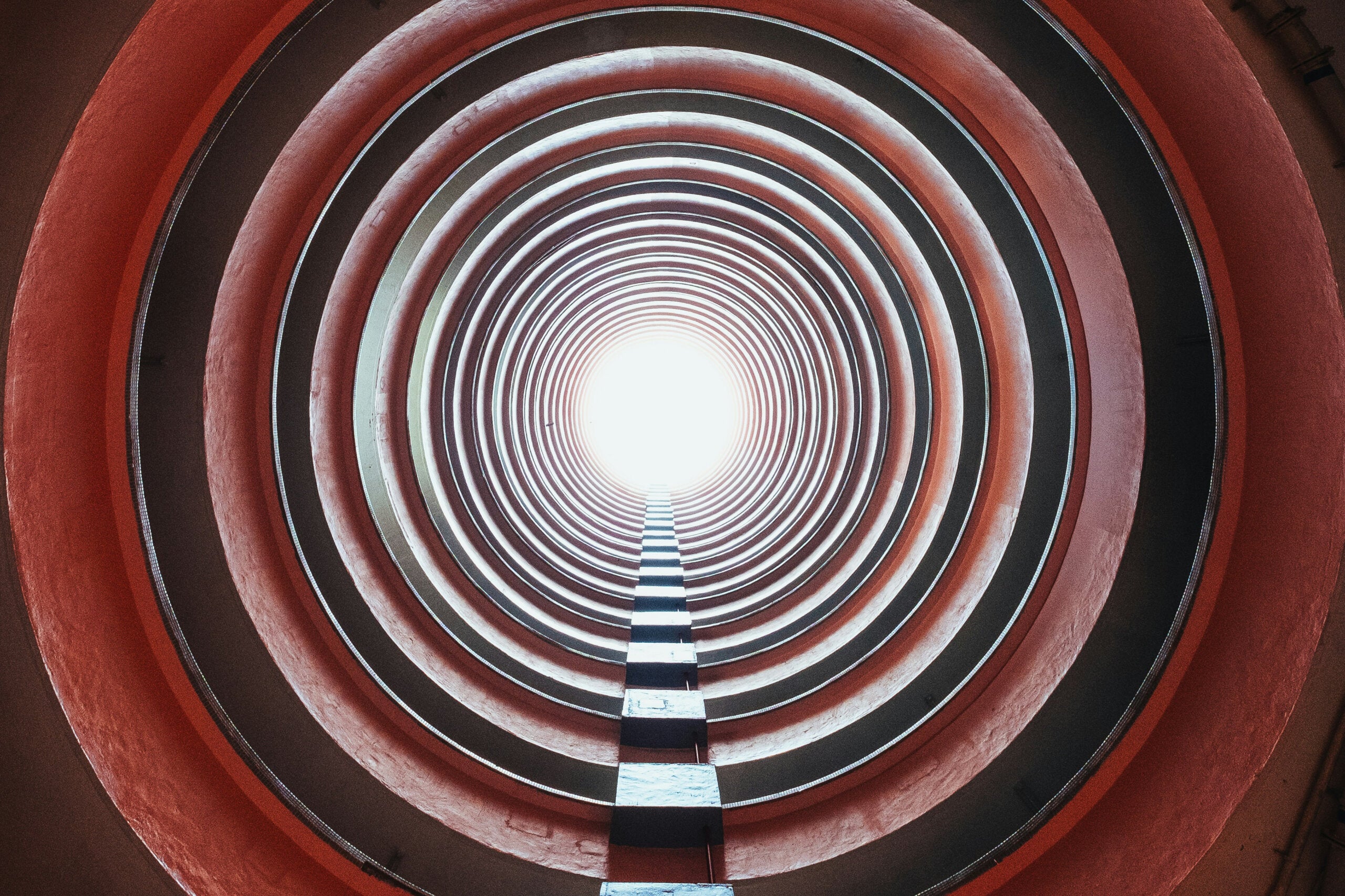 A corrugated red and black tunnel with light at the end.